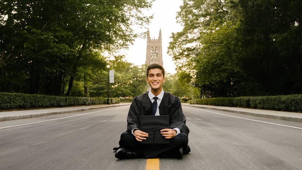 Man, sitting with graduation robes, Duke chapel in distance