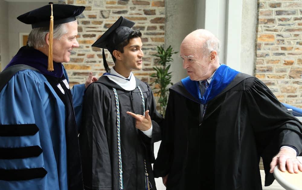 Young man in cap and gown, with two other older people in caps and gowns look on