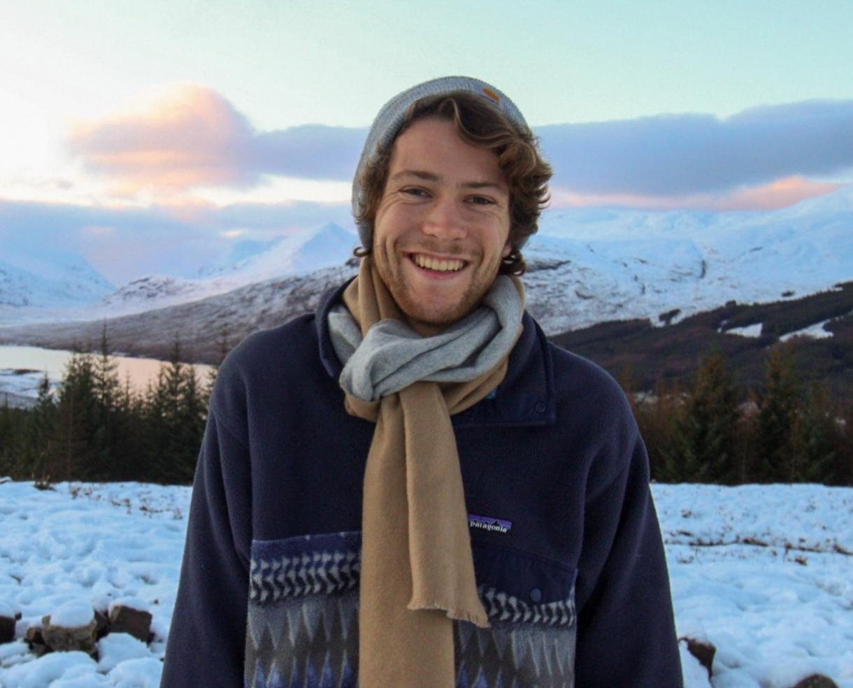 man smiling in front of a snowy mountain background