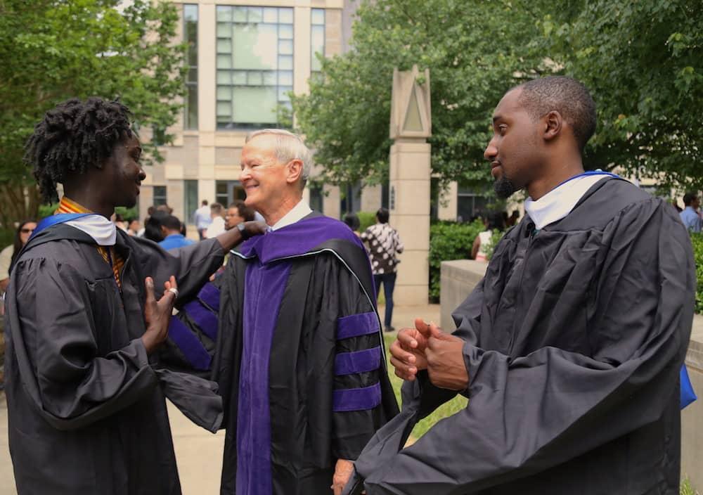 Man with white hair in graduation gown congratulating two men