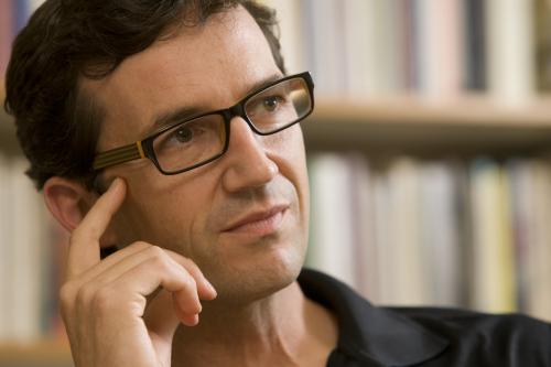 Man with glasses holding his hand to his face while looking into the distance