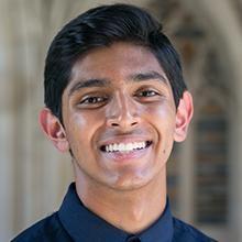 Shivam Patel smiling in front of a stone and brick background.