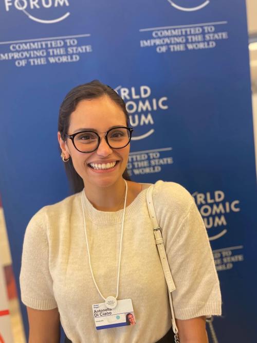 Woman, brown hair and glasses smiling in front of World Economic Forum banner