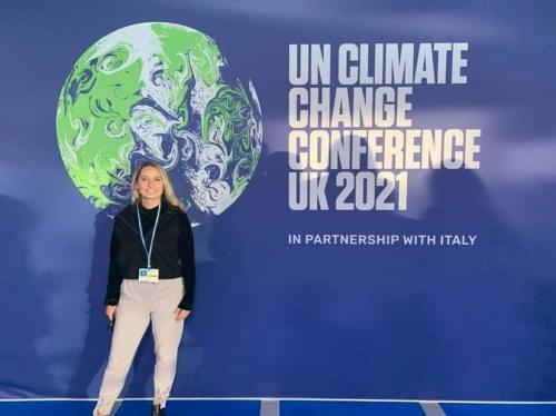 Woman standing in front of large wall that has a globe and a sign that. says "UN Climate Change conference 2021"