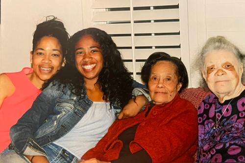 Woman sitting on couch with her mother, grandmother, and great grandmother.