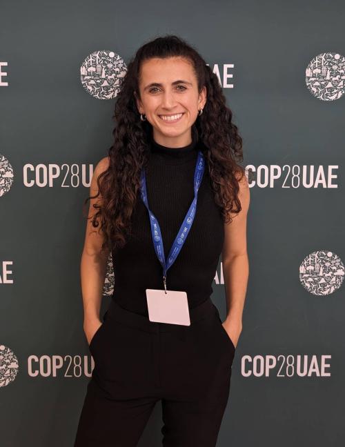Woman in front of COP28UAE sign, smiling, hands in pockets