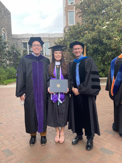 Three people standing in regalia after graduation. 