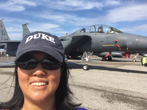 Lan wearing Duke hat in front of fighter jet