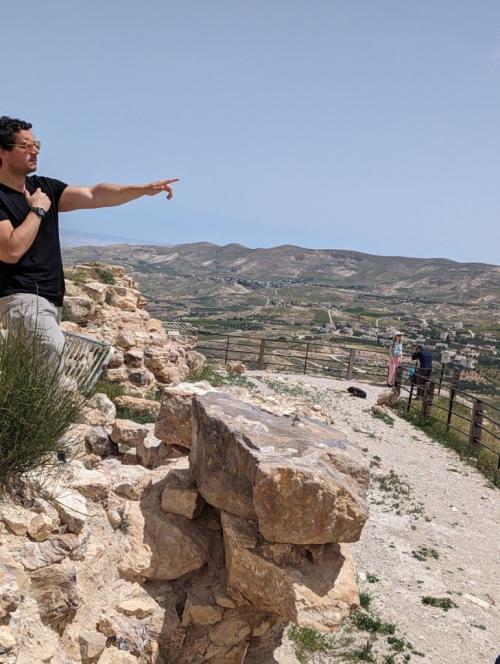 Man pointing into distance while standing on top of rocky area. 