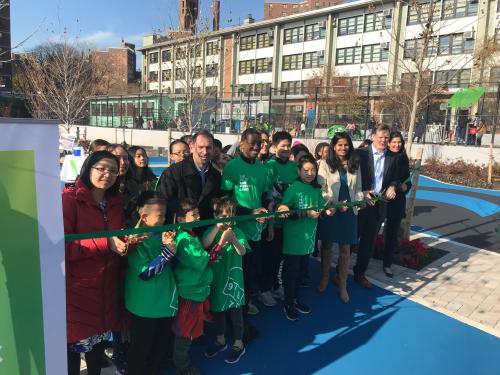 A crowd of people cut a ribbon together to introduce new climate resilient playground.