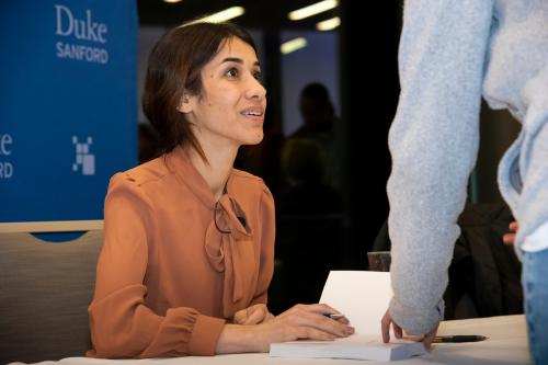 woman in a orange blouse signing a book